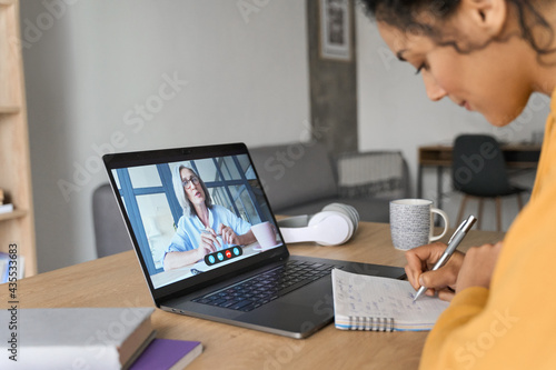 Fotografía African American mixed race adult student having virtual meeting online call educational webinar chatting with senior teacher at home office writing notes