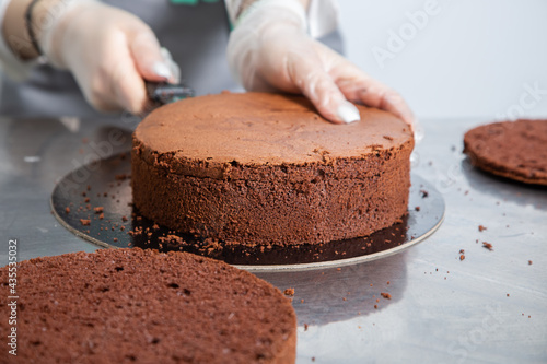 Womans hands chef cutting chocolate cake layers and stacking them on metal table