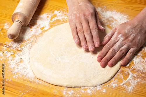 Hands with rolling-pin make dough for pizza. Italian pizza cooking preparation process on wood table. Pizza dough