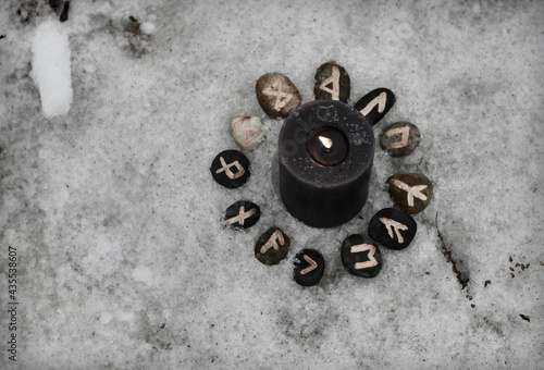 Top view of black burning candle with runes and copy space against snow.