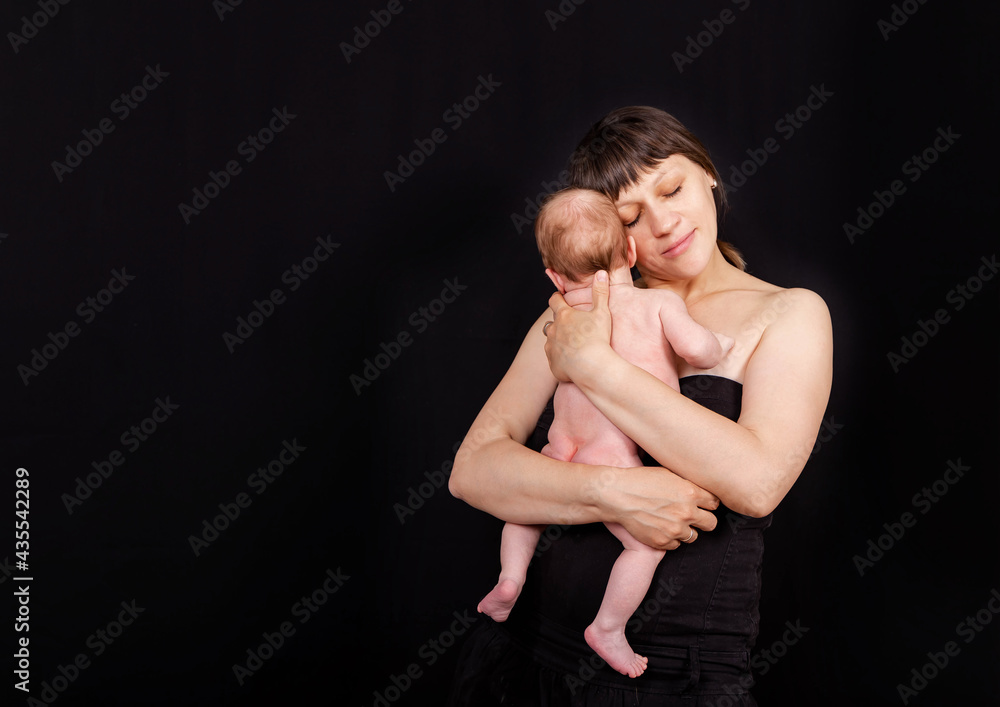 Naklejka premium Newborn baby with mommy. Love of a mother and baby. Family. Smiling baby and his mom. Young mother holding her newborn child in hands. Caucasian mom holding her cute infant on the black background.