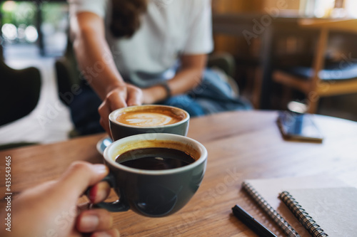 Closeup image of a man and a woman clinking white coffee mugs in cafe