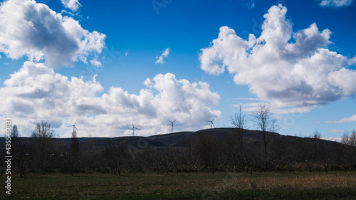 Rural landscape with windmills on the top of the hill. Fruit orchards and agricultural fields in the foreground.