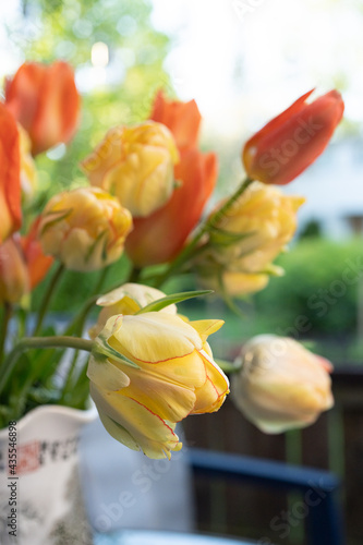 Yellow and orange tulips on the table in a vase. Summer on the balcony.