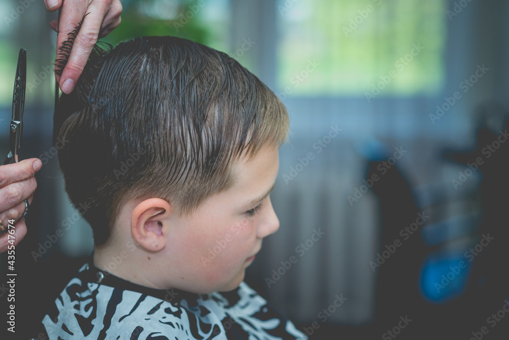 Cute little boy getting haircut by hairdresser at the barbershop.Side view.Closeup.Toned. Cute little boy getting haircut by hairdresser at the barbershop.Side view.Closeup.Toned.