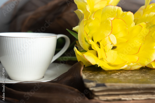 Still life. Yellow and orange tulips, cup of coffee and old book. Concept of congratulation