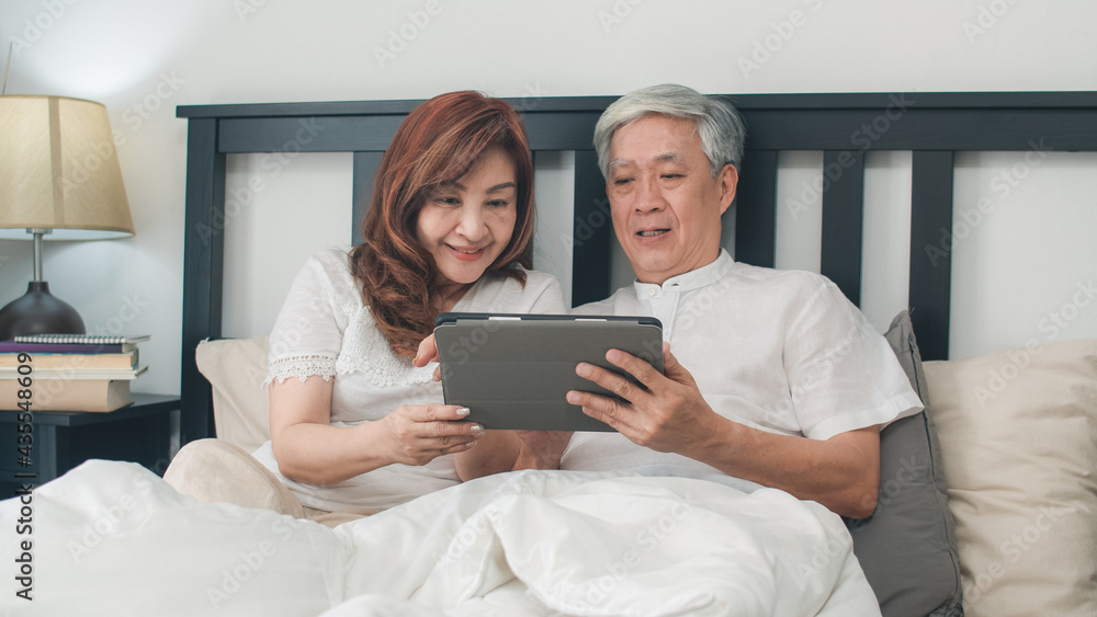Asian senior couple using tablet at home. Asian Senior Chinese grandparents, husband and wife happy after wake up, watching movie lying on bed in bedroom at home in the morning concept. Asian senior couple using tablet at home. Asian Senior Chinese grandparents, husband and wife happy after wake up, watching movie lying on bed in bedroom at home in the morning concept.