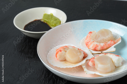 Natural raw scallop with boiled shrimp in the sink in a ceramic bowl with soy sauce and wasabi on a dark background.
