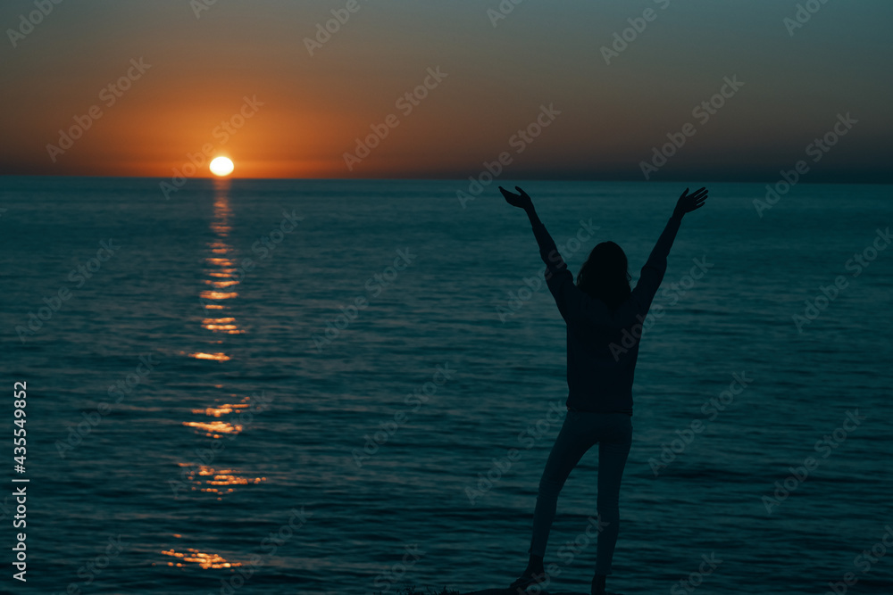 woman in the mountains at sunset near the sea raised her hands up
