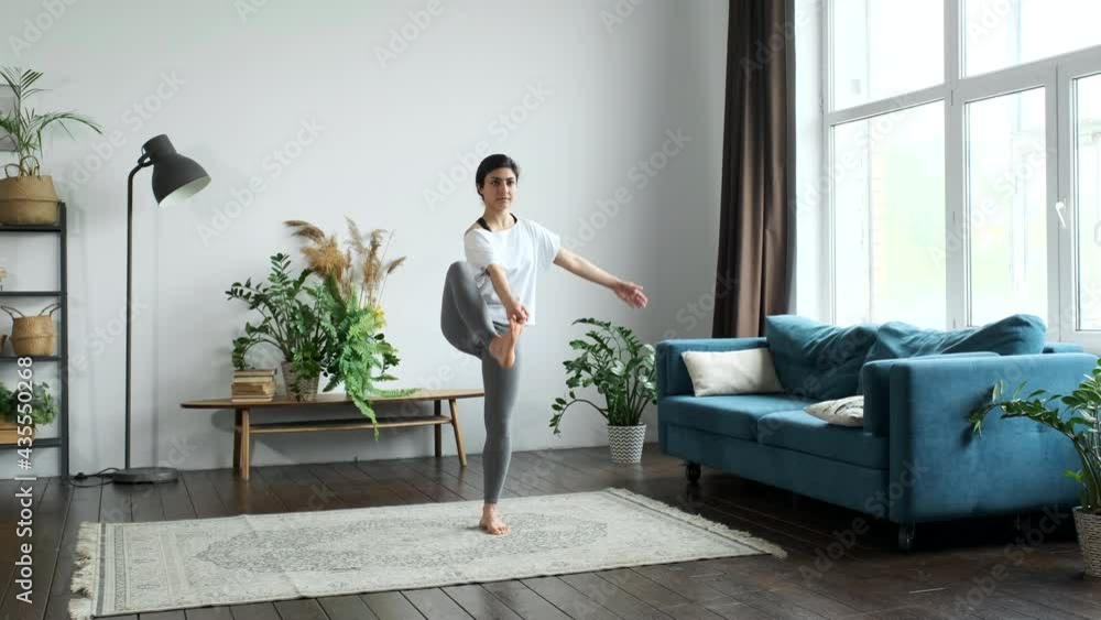 A Young Indian Woman Is Doing Yoga, Doing The Exercise Standing on One Leg For Balance. Located at Home in a Bright Room A Young Indian Woman Is Doing Yoga, Doing The Exercise Standing on One Leg For Balance. Located at Home in a Bright Room
