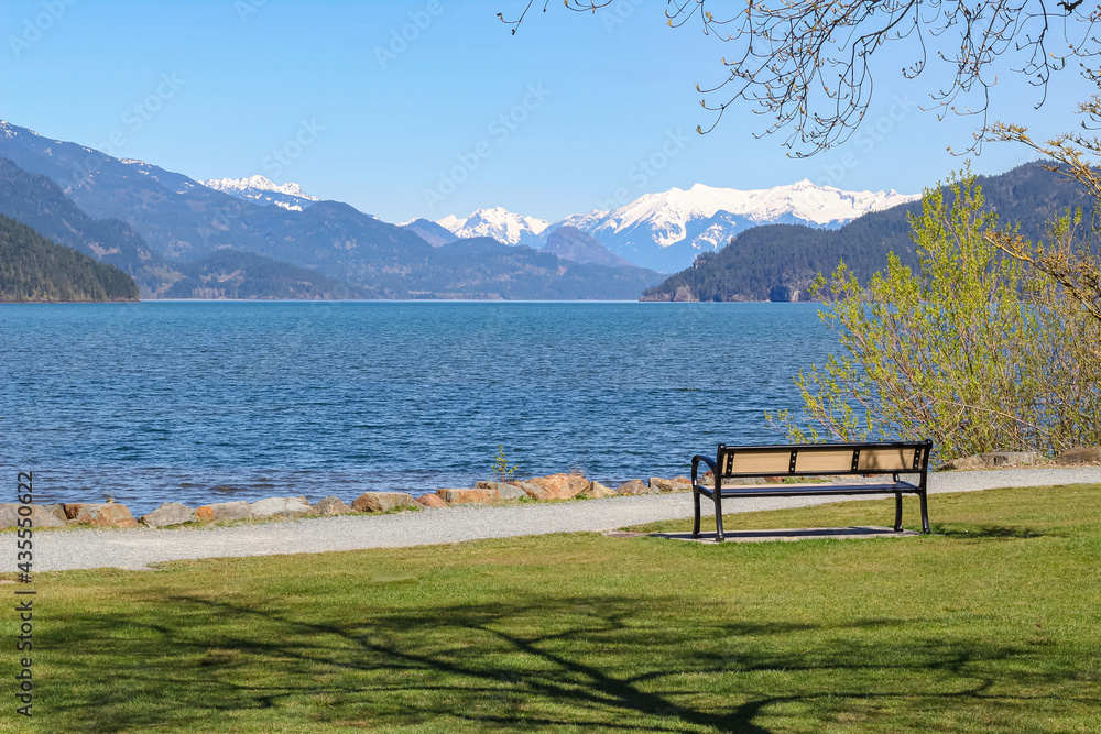 Beautiful landscape of the Harrison Lake and mountains on the background. Empty bench on the beach of the lake.