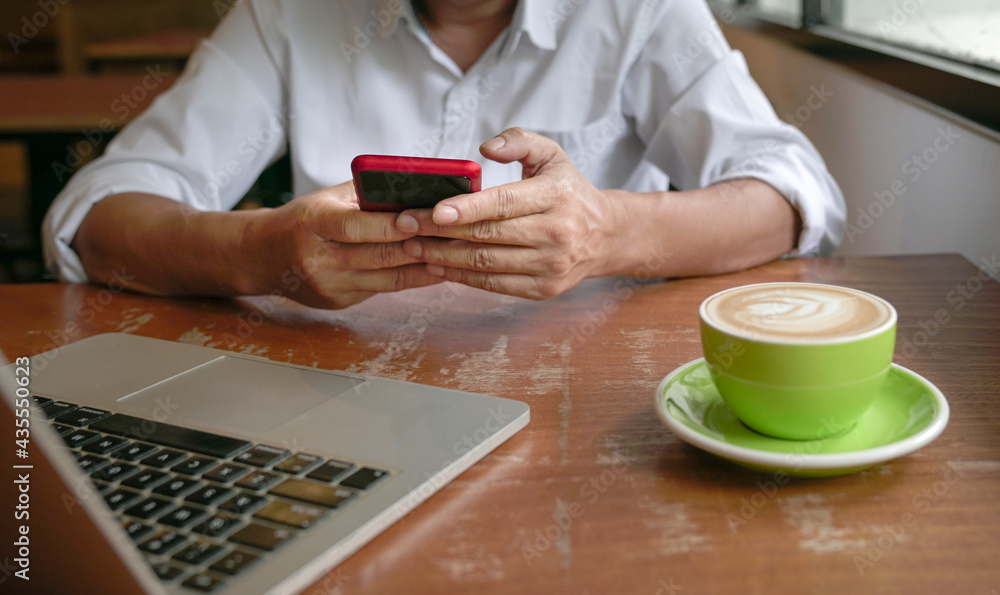 Man reading phone with computer and cup of coffee on table. Man reading phone with computer and cup of coffee on table.