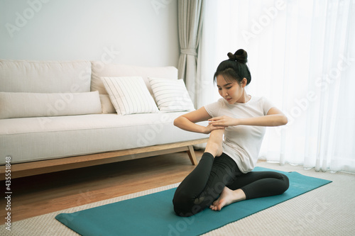 Portrait of gorgeous young asian woman practicing yoga at home stretching out while following a yoga routine.