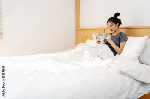 happy Young asian woman  holding cellphone  in bed