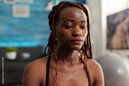 Photos Black woman training body and mind meditating in lotus pose keeping eyes closed, sitting on yoga mat in home living room for calm, healthy harmony lifestyle dressed in sportwear