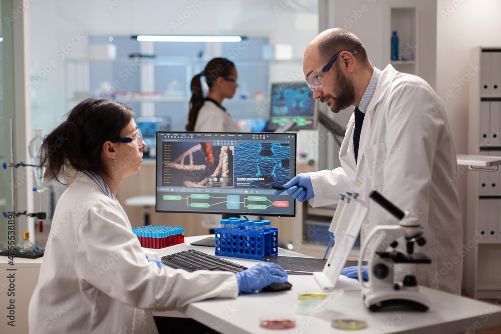 Scientist woring together to find a vaccine in healthcare lab looking at dna sample on computer. Chemists stuff analysing virus evolution using high tech technology for treatment research. Scientist woring together to find a vaccine in healthcare lab looking at dna sample on computer. Chemists stuff analysing virus evolution using high tech technology for treatment research.