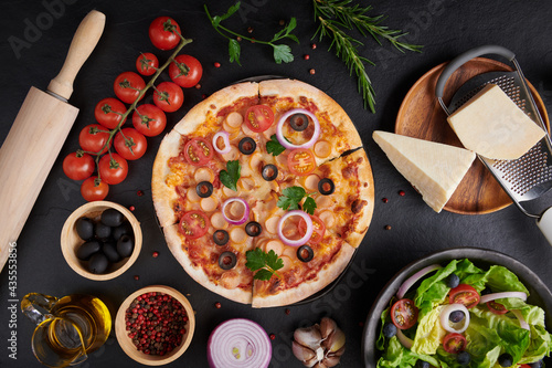 assorted foodset on table. Italian pizza and pizza cooking ingredients on dark stone background. tomatoes on vine, mozzarella, black olives, herbs and spices, vegetable salad. top view. photo