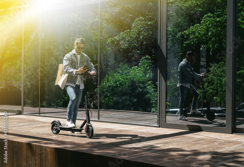The guy is riding an electric scooter against the background of the city. Using iPhone.
