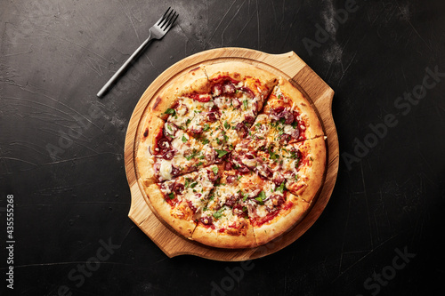 pizza on a wooden base on a black textured background top view