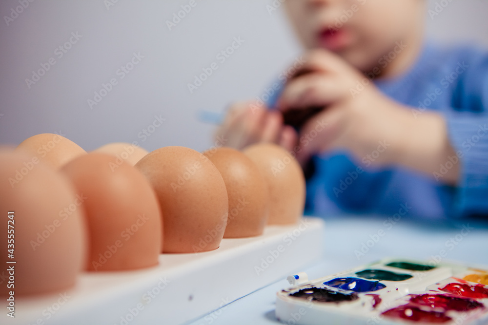 A little child paints an easter egg at the table on a blue background.Little Boy painting Easter Eggs with Paint at Home. Children's Easter creativity. A child decorate Easter eggs. A little child paints an easter egg at the table on a blue background.Little Boy painting Easter Eggs with Paint at Home. Children's Easter creativity. A child decorate Easter eggs.