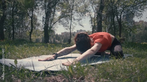 A young woman does a stretching exercise, fitness, yoga on the street on a mat in the forest in a clearing. Sport. Sonce grass, lake. The general plan. He smiles. On the background of the house. View  photo