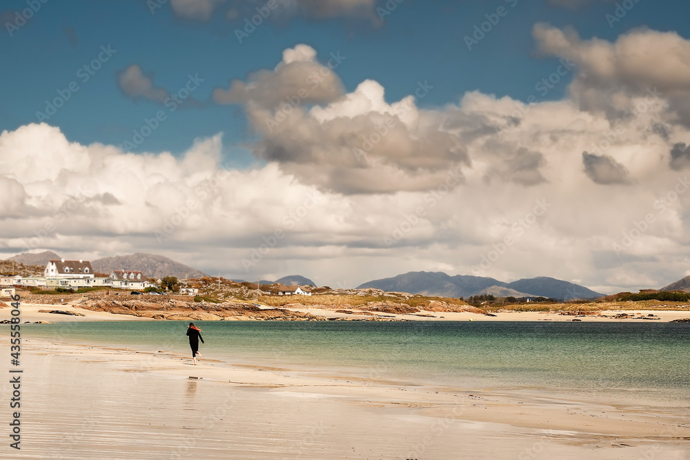 Young teenager girl walking on a warm sand of Gurteen beach, county Galway, Ireland. Warm sunny day. Cloudy sky. Outdoor activity concept. Beautiful Irish scenery in the background