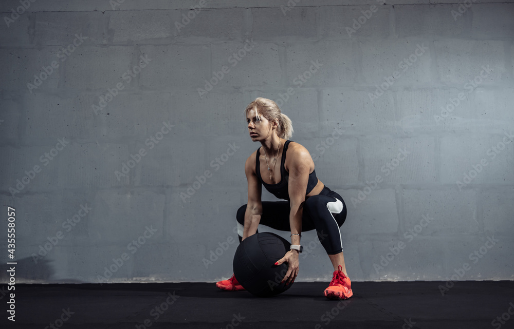 Sportswoman doing stretching exercise with medicine ball. Muscular woman exercising fitness ball at gym