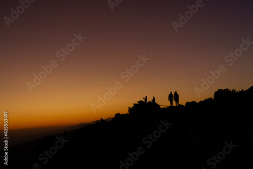 Medium shot of silhuette of people standing against orange colorful sunset sky in joshua tree national park in america