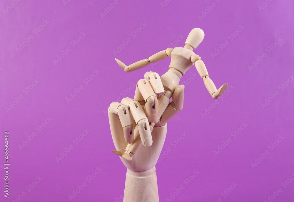 Wooden hand holding wooden puppet on purple background Wooden hand holding wooden puppet on purple background