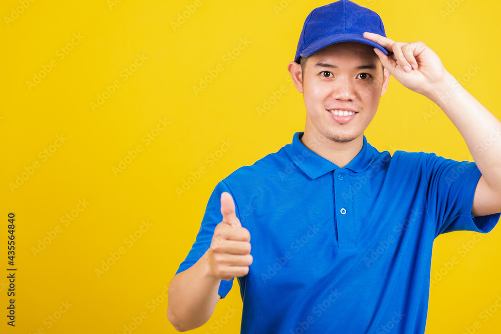 Portrait professional attractive delivery happy man standing he smile wearing blue t-shirt and cap uniform showing thumb up gesture looking to camera, studio shot isolated on yellow background Portrait professional attractive delivery happy man standing he smile wearing blue t-shirt and cap uniform showing thumb up gesture looking to camera, studio shot isolated on yellow background