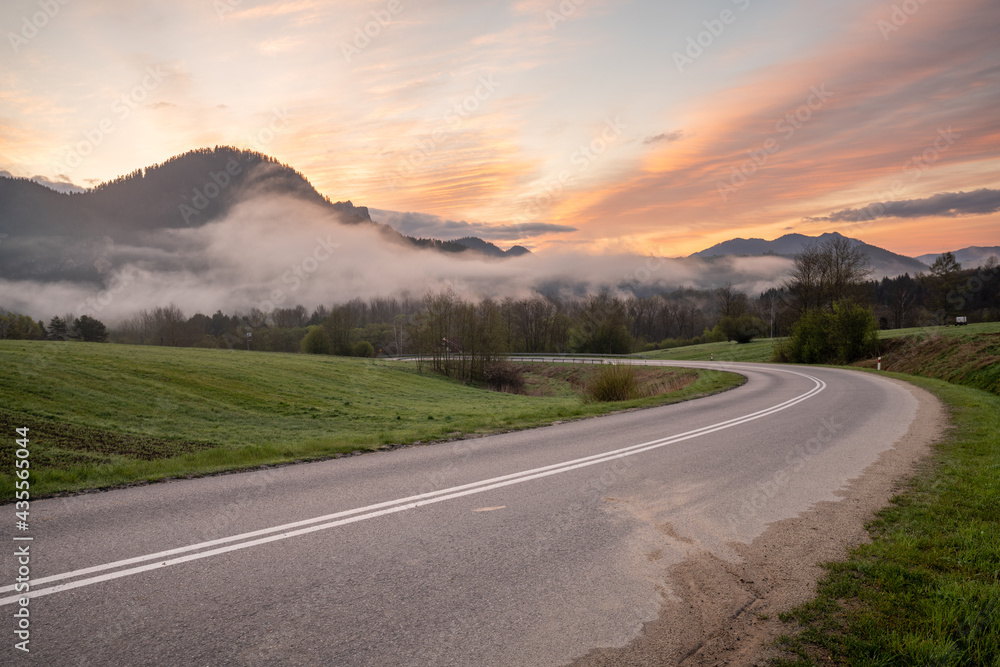 Fototapeta premium An asphalt road in the mountains during a beautiful, foggy and sunny morning