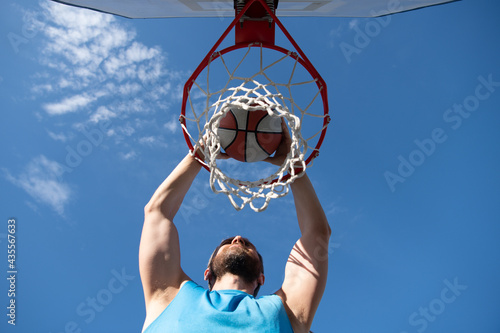 Close up image of professional basketball player making slam dunk during basketball game in outdoor basketball court.