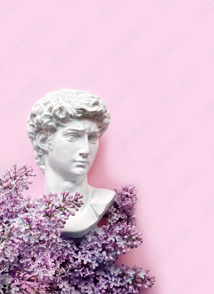 Plaster head of David and lilac flowers on violet background. floral composition with Gypsum copy of antique statue. spring season. modern style. creative minimal art concept. flat lay