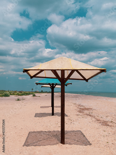 Wooden umbrellas on white sand beach with harsh shadows  vivid blue sea water cloudy sky background. Scenic landscape wallpaper summer vacation seasonal tropical marine travel rest resort advertising.