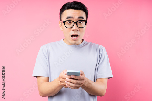 Portrait of Asian man using smartphone on pink background © Timeimage