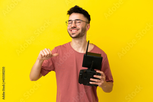 Man holding a drone remote control isolated on yellow background proud and self-satisfied