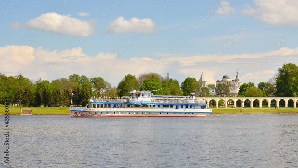 Naklejka premium A ship is sailing along the coast, a colonnade stretches along the embankment, and the domes of temples are visible in the future. Velikiy Novgorod.