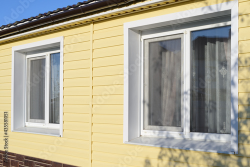 The wall of a private house with plastic windows covered with yellow vinyl siding