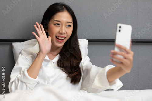young beautiful woman sitting on bed, taking photo, selfie or talking online to someone from smartphone