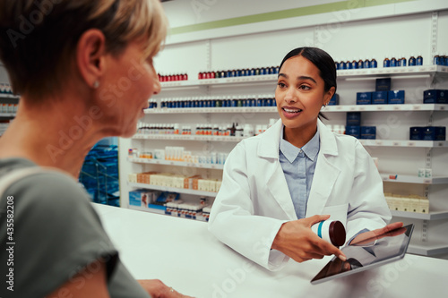 Fototapet Female pharmacist guiding customer with tablets by showing something on digital