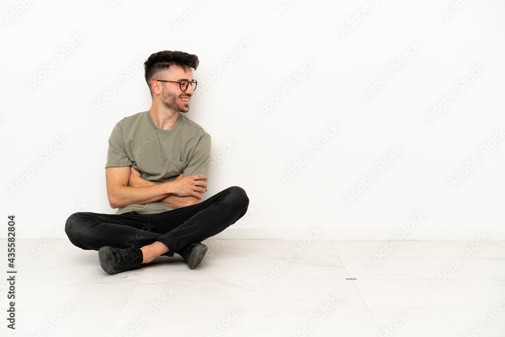 Young caucasian man sitting on the floor isolated on white background looking side Young caucasian man sitting on the floor isolated on white background looking side