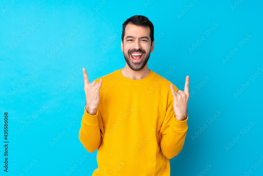 Young caucasian man over isolated blue background making rock gesture Young caucasian man over isolated blue background making rock gesture