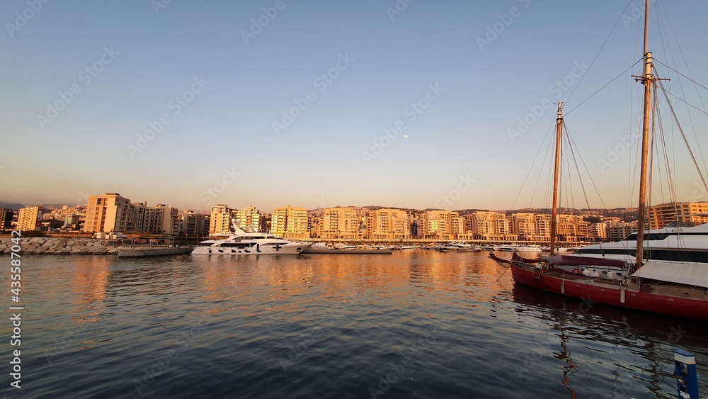 Naklejka premium Sunset at the port with boats and buildings. City view from the sea. Tranquil scene in the evening. Travel destination and vacations