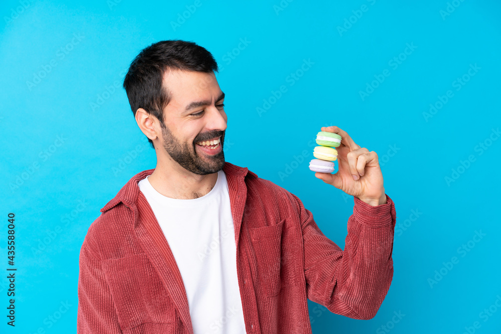 Young caucasian man over isolated blue background holding colorful French macarons and happy Young caucasian man over isolated blue background holding colorful French macarons and happy