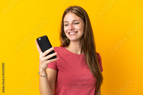 Young woman using mobile phone isolated on yellow background with happy expression