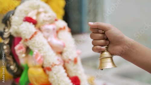 Close up of hand offering prayer by using Brass bell or Ghanti while worshipping lord Ganesha during festival photo