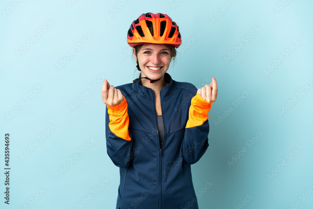 Young cyclist woman isolated on blue background making money gesture Young cyclist woman isolated on blue background making money gesture