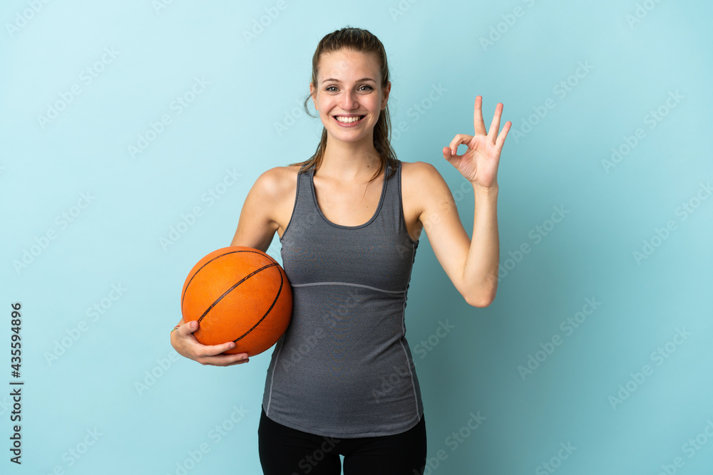 Young woman playing basketball isolated on blue background showing ok sign with fingers