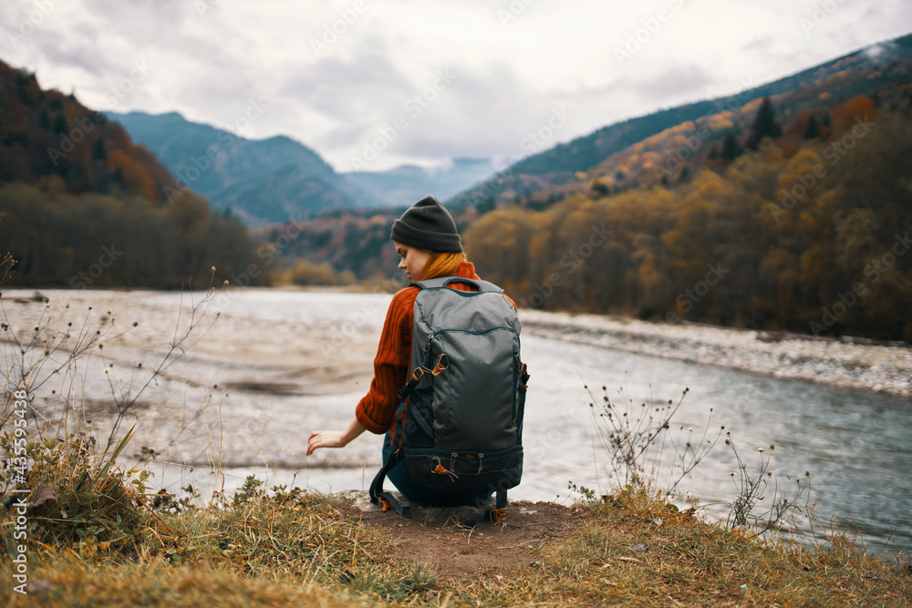 Fototapeta premium woman hiker on the banks of the river in autumn and mountains in the distance clouds weather nature