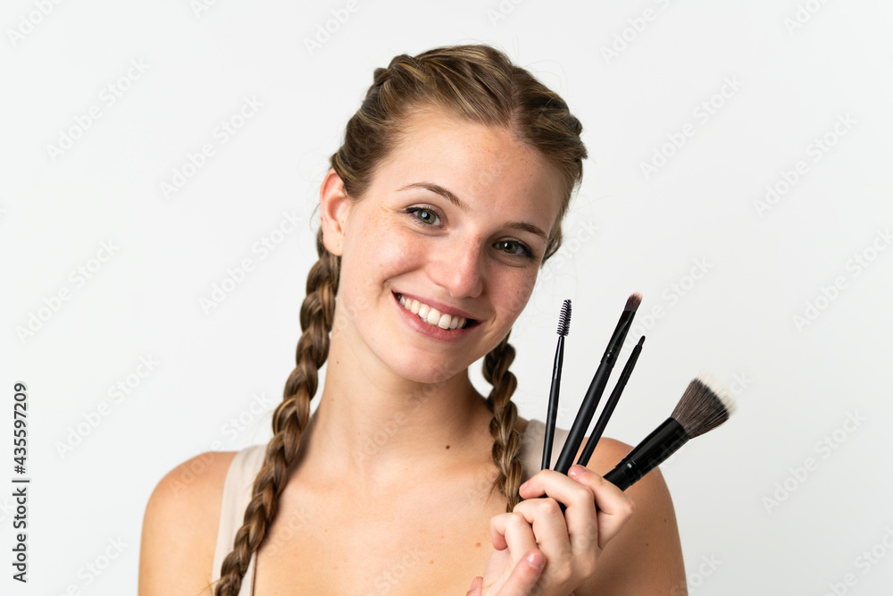 Obraz premium Young caucasian woman isolated on white background holding makeup brush and whit happy expression